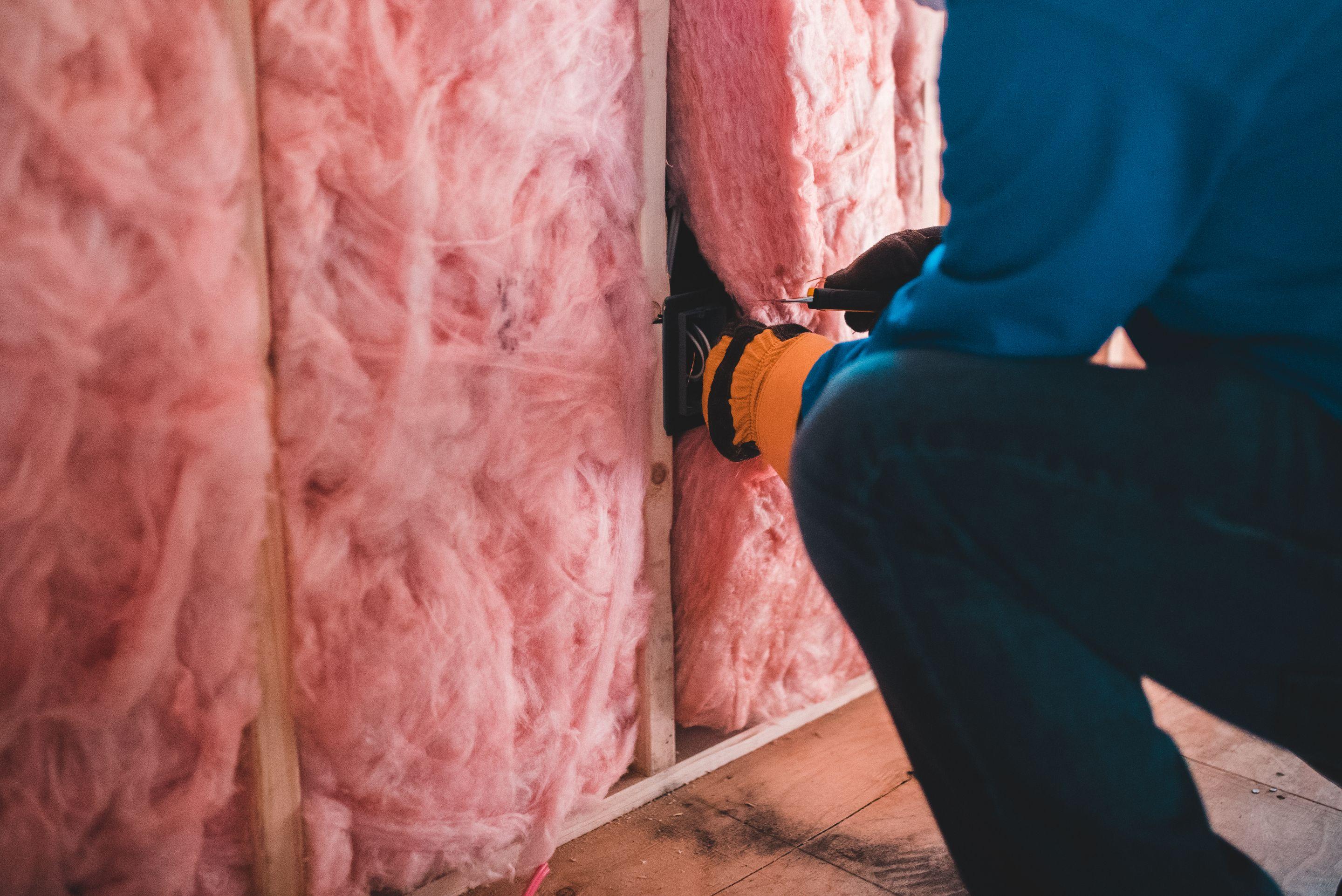 Insulation installer fitting pink fiberglass batt insulation between roof rafters