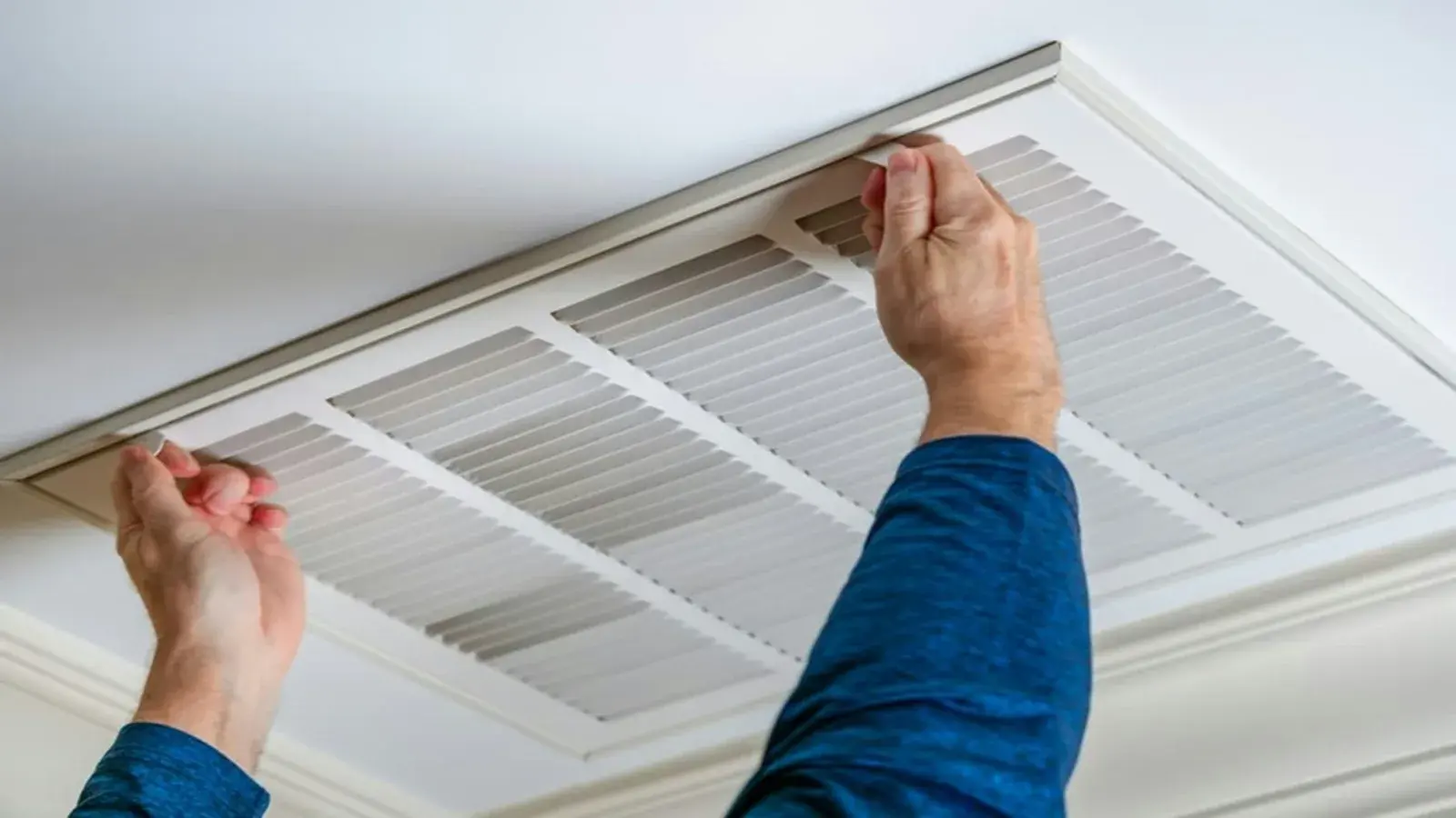 Technician servicing a ceiling-mounted air conditioning duct unit